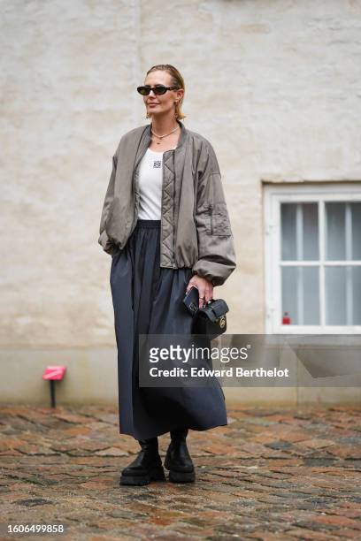 Guest wears black sunglasses, a gold chain with logo pendant earrings from Valentino, a white pearls necklace, a white tank-top from Loewe, a gray...
