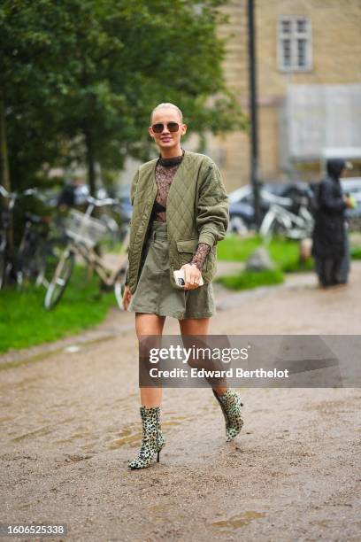 Guest wears black aviator sunglasses, a black lace print pattern long sleeves t-shirt, a khaki quilted jacket, a khaki short skirt, white socks, pale...