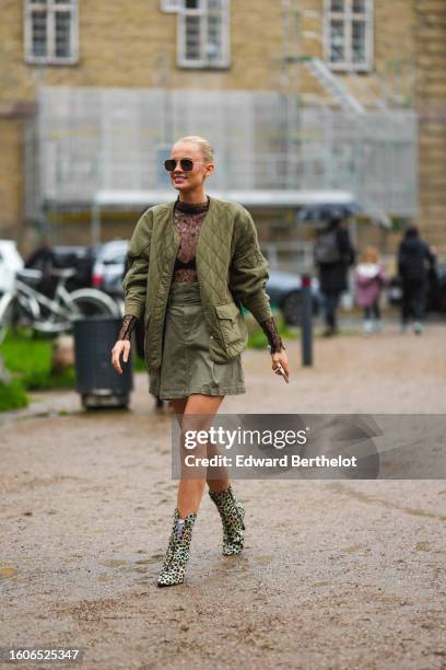 Guest wears black aviator sunglasses, a black lace print pattern long sleeves t-shirt, a khaki quilted jacket, a khaki short skirt, white socks, pale...
