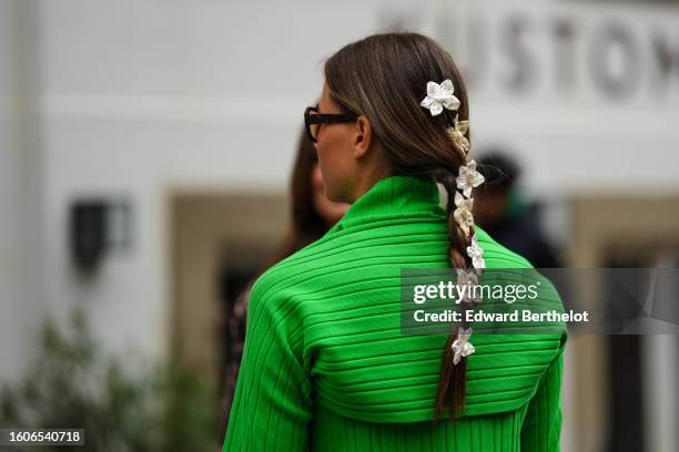 Guest wears white and black flower hair clips, brown marble print pattern sunglasses, a neon green embossed striped pattern top, outside Baum und...