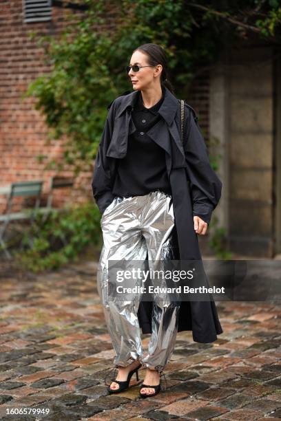 Guest wears black sunglasses, a black buttoned polo shirt, a black long coat, silver shiny cargo large pants, black open toe-cap heels mules ,...