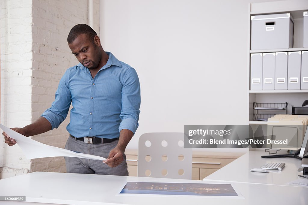 Black architect looking at blueprints in office