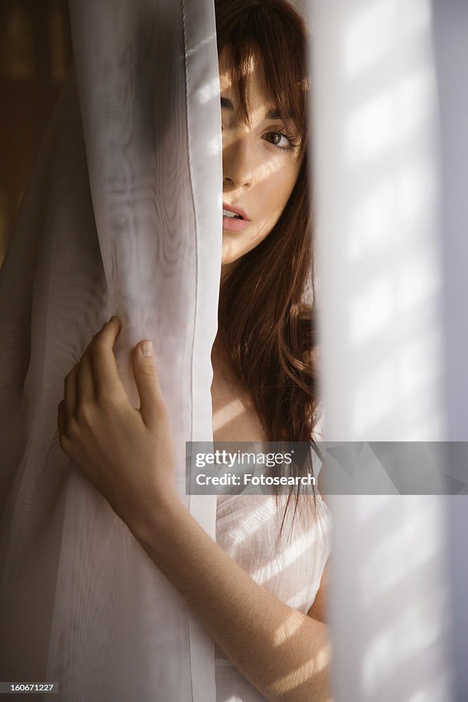 Woman standing in sunlit curtains