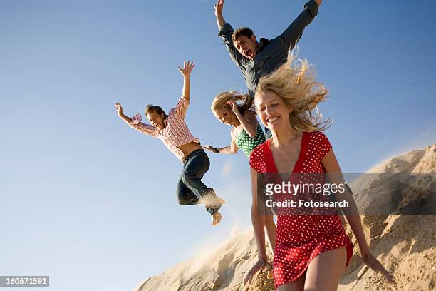 two couples on beach jumping off sand dune - sand dune stock pictures, royalty-free photos & images