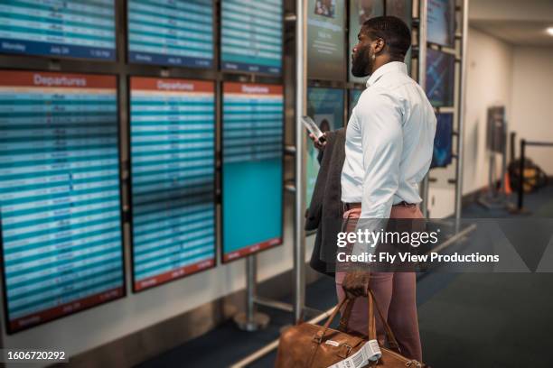 mann im flughafen liest die ankunfts-/abflugtafel - ankunfts und abfahrtstafel stock-fotos und bilder