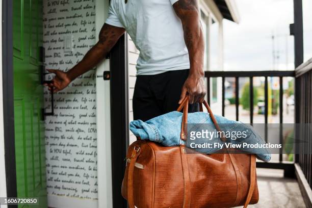 man with duffel bag closes front door behind him - duffel tas stockfoto's en -beelden