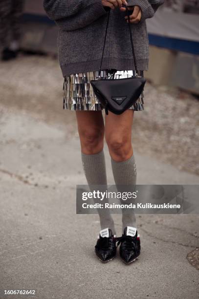 Guest wears a sweater, metal silver skirt from Muntche, long grey socks, black shoes and a black triangle Prada bag during the Copenhagen Fashion...