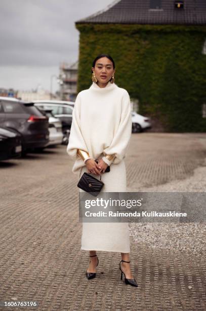 Guest wears cashmere jumper, golden earrings, bracelets, black bag, skirt, heels outside Munthe during the Copenhagen Fashion Week Spring/Summer 2024...