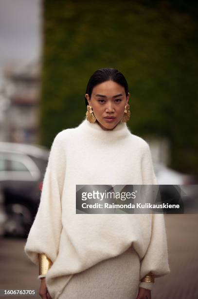 Guest wears cashmere jumper, golden earrings, bracelets, black bag, skirt, heels outside Munthe during the Copenhagen Fashion Week Spring/Summer 2024...