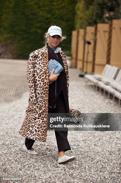 Karin Teigl wears a cap, Chanel bag in a blue, black oversized blazer, pants, and coat with animal print outside Munthe during the Copenhagen Fashion...