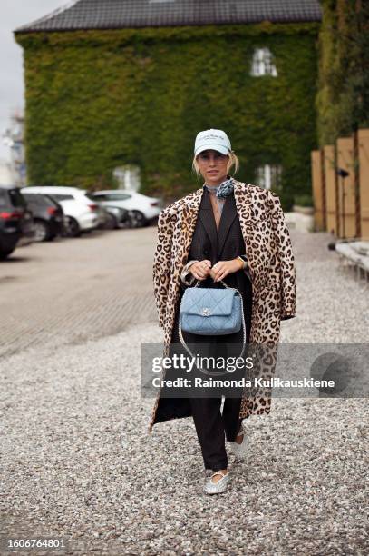 Karin Teigl wears a cap, Chanel bag in a blue, black oversized blazer, pants, and coat with animal print outside Munthe during the Copenhagen Fashion...