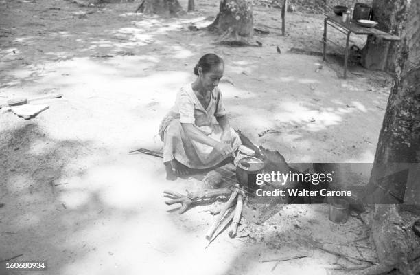 Brazil. Brésil- Période 1950-1955- Reportage sur le Brésil: dans un village en forêt, une femme âgée assise en tailleur au sol fait cuire un met dans...