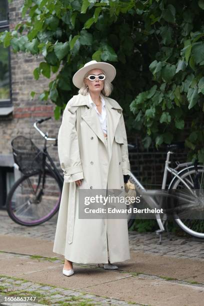 Guest wears a beige felt wool large hat, white socks, a white cropped shirt, a beige long trench coat, a pale yellow braided leather Jodie handbag...