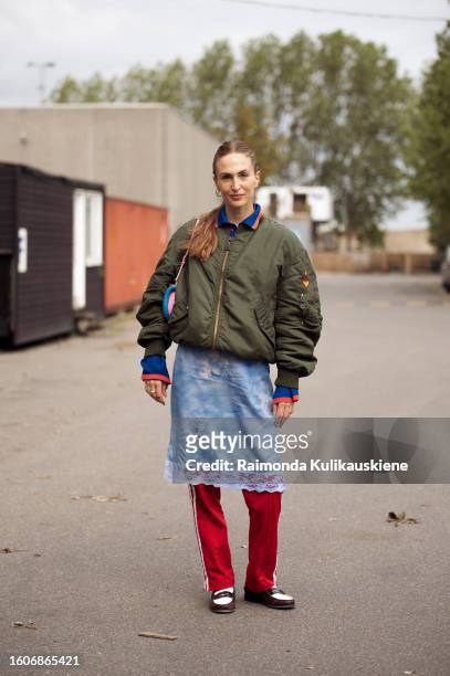 Guest wears red pants, a blue dress, and an army green jacket outside Helmstedt during the Copenhagen Fashion Week Spring/Summer 2024 on August 10,...
