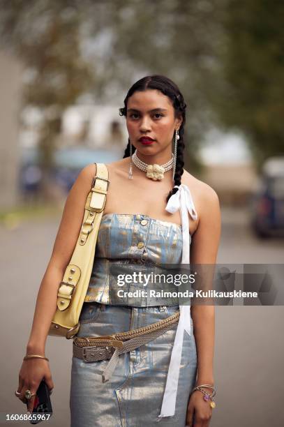 Guest wears a metal imitation midi skirt and top, yellow bag, and black long leather boots outside Helmstedt during the Copenhagen Fashion Week...