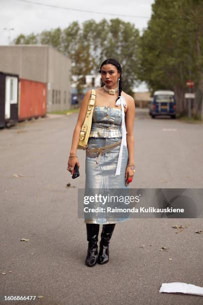 Guest wears a metal imitation midi skirt and top, yellow bag, and black long leather boots outside Helmstedt during the Copenhagen Fashion Week...