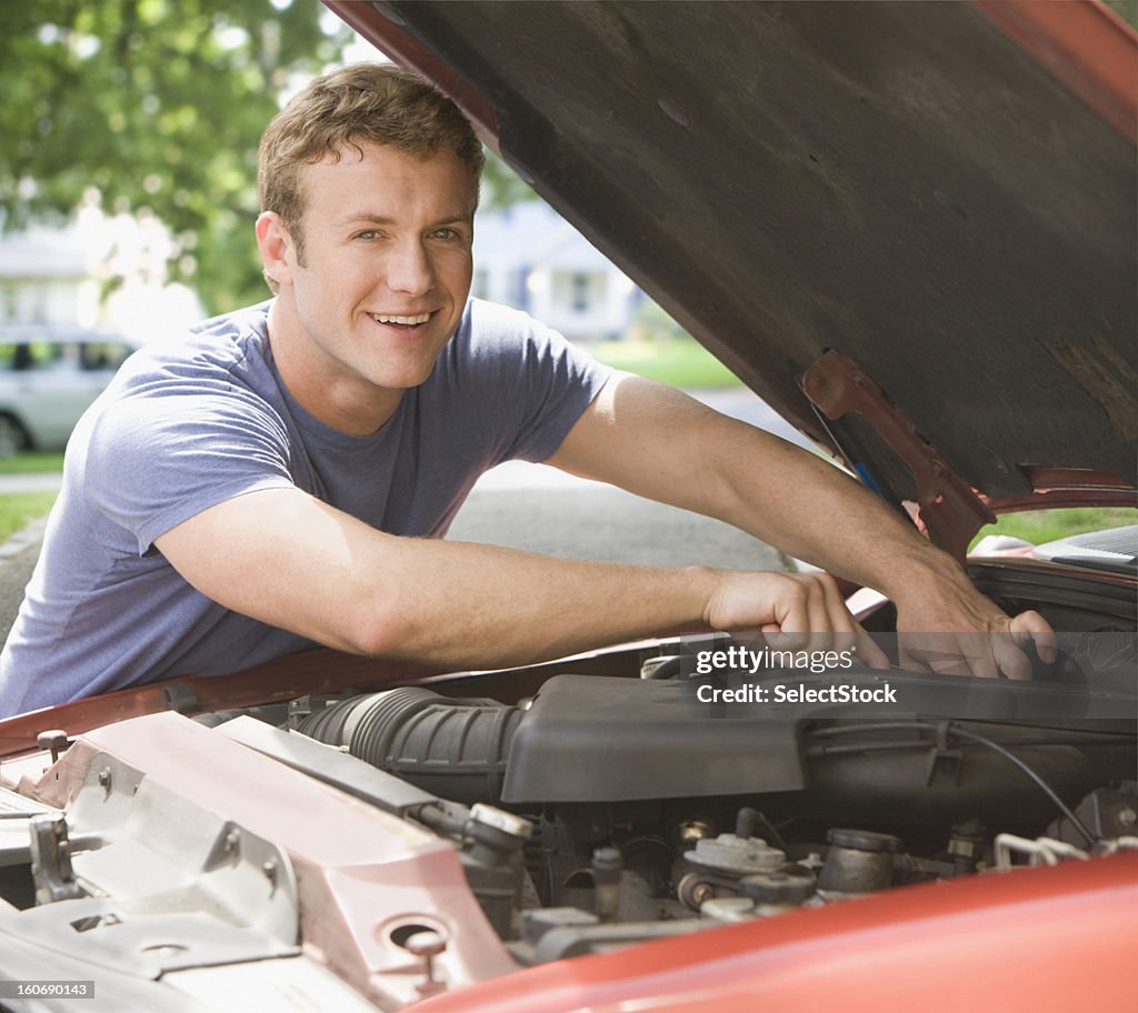 Young man fixing engine of his car smiling