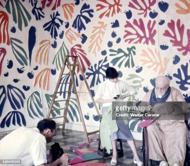 Henri Matisse In Nice. Henri MATISSE assis dans un fauteuil roulant, découpant des morceaux de papiers de couleurs avec son assistante, dans son...