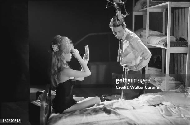 Shooting Of The Film 'la Bride Sur Le Cou' By Roger Vadim. Brigitte BARDOT de profil, assise sur un lit, arrangeant sa coiffure en se regardant dans...