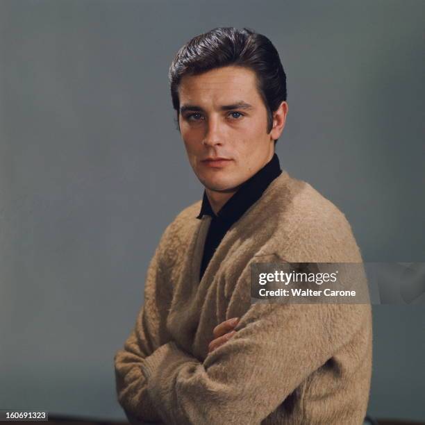 Close-up Of Alain Delon. Photo studio : plan de face souriant d'Alain DELON les bras croisés sur fond gris.