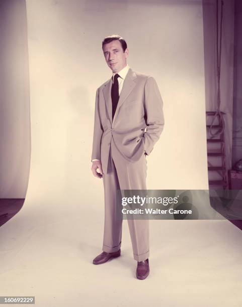 Yves Montand. Lors d'une scéance en studio, l'acteur Yves MONTAND, en costume gris-clair et cravate noire, se tient debout, la main gauche dans la...