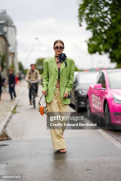 Guest wears black squared sunglasses, gold and red rhinestones earrings, a navy blue denim ripped large flower necklace, a black denim shoulder-off /...