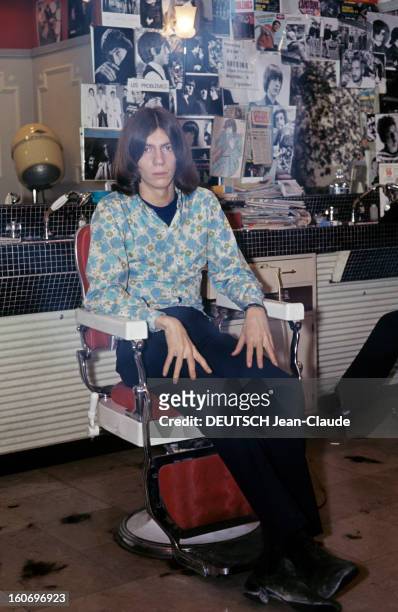Close-up Of Antoine. ANTOINE, cheveux mi-longs, vêtu d'une chemise à fleurs dans les tons bleu et vert, pose assis sur le fauteuil d'un salon de...
