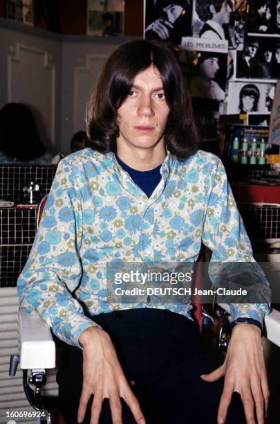 Close-up Of Antoine. ANTOINE, cheveux mi-longs, vêtu d'une chemise à fleurs dans les tons bleu et vert, pose assis sur le fauteuil d'un salon de...