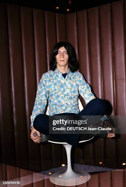 Close-up Of Antoine. ANTOINE, cheveux mi-longs, vêtu d'une chemise à fleurs dans les tons bleu et vert, pose assis en posture yoga 'lotus'.