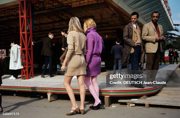 Fashion Mini Skirt. Deux mannequins en mini jupe beige et violet passent aux abords d'un stand d'une fête foraine, sous le regard appuyé de deux...