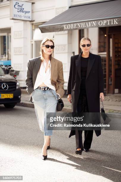 Annabel Rosendahl wears a denim skirt, white shirt, brown blazer, and black bag and Tine Andrea Lauvli wears black pants, black top, and long black...