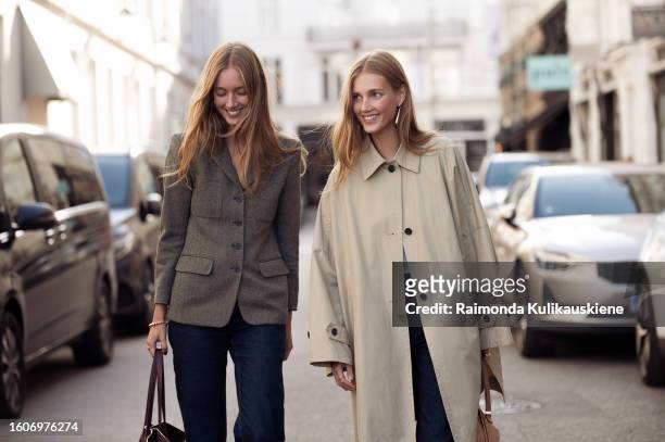 Amalie Moosgaard wears black pants, a brown jacket, and a brown bag, and Cecilie Moosgaard wears black wide pants, and a beige trench coat and beige...