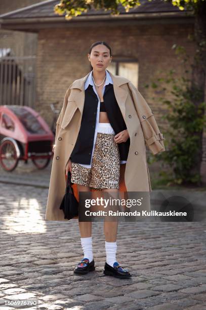 Steph wears animal prints wide shorts, white underwear, black bikini top. Blue shirt, black sweater, beige trench coat, white socks, and black...