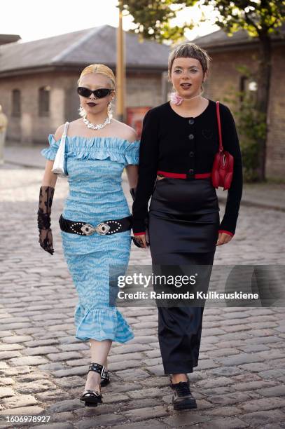 Fumina T. Wears a long blue dress, black gloves, black belt, and black belt and Emma Fridsell wears a long black skirt a black cropped jacket, and a...