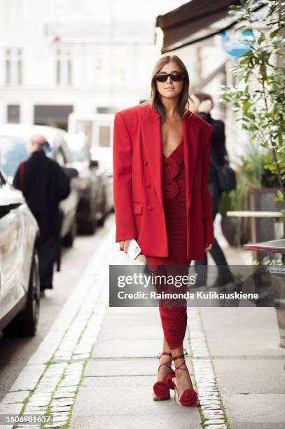 Darja Barannik wears a red dress, red oversized jacket, red summer shoes with roses, and black sunglasses outside Rotate during the Copenhagen...