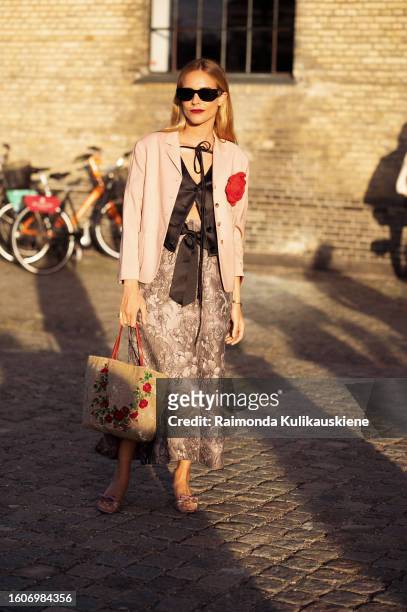 Blanca Miro Scrimieri wears a beige maxi skirt, black sheer blouse, pink blazer with a red flower, and black sunglasses outside Ganni during the...
