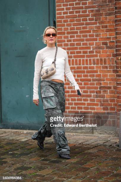 Guest wears brown marble print pattern squared sunglasses, gold earrings, a white transparent wool long sleeves t-shirt, a beige sheep fur crossbody...