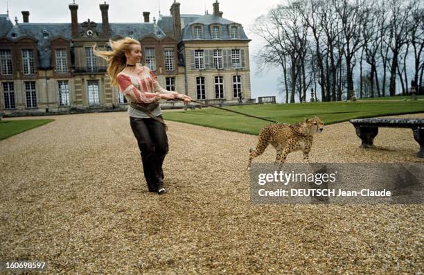 Rendezvous With Anne Gael. Anne GAEL, cheveux longs, au vent, portant une blouse rose et un pantalon noir, court en tenant en laisse un léopard dans...