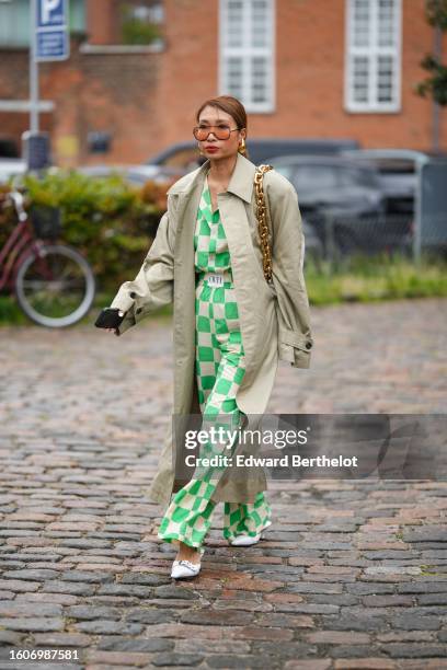 Guest wears orange large sunglasses, a beige trench coat, a white latte and green checkered print pattern shirt from OVH, matching beige and green...