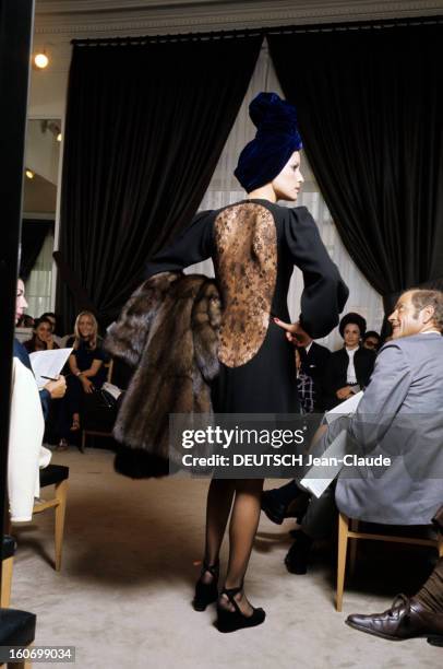 The House Of Couture Yves-saint-laurent In Paris. Un mannequin, portant une robe noire unie, dont le dos est réalisé en dentelle noire dessinant une...