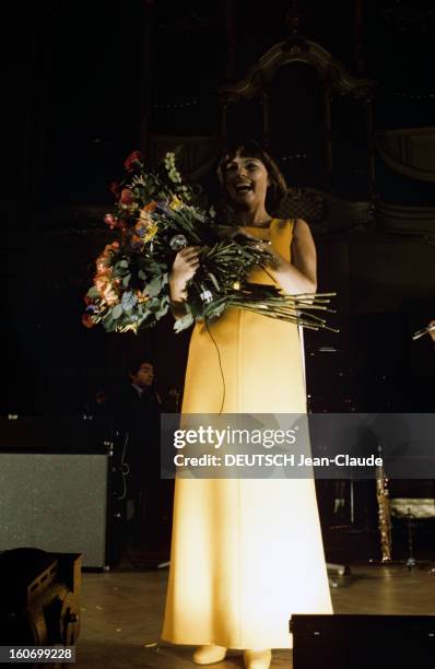 Close-up Of Mireille Mathieu In Gdr . RDA- 1972- Mireille MATHIEU, debout sur la scène, en robe blanche, rit aux éclats, un bouquet de fleurs énorme...