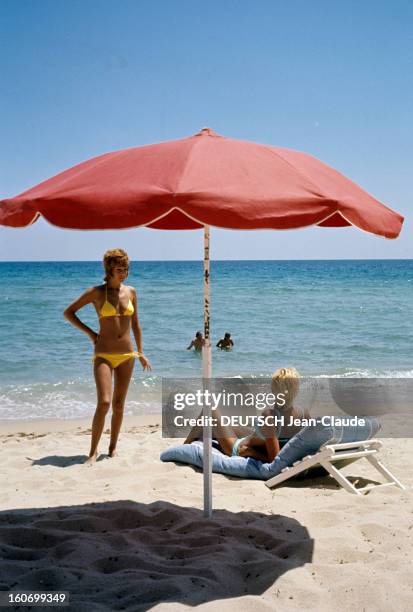 Naiads Are Back. Saint-Tropez, juillet 1971- Reportage sur les naïades de la plage: Un parasol rouge planté dans le sable en premier-plan, en...
