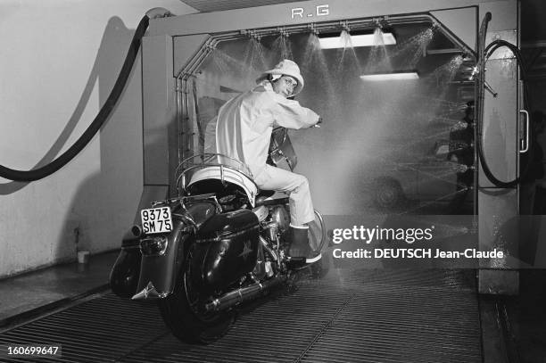 Close-up Of Jacques Dutronc. Jacques DUTRONC, dans un garage, sur une moto , en ciré imperméable et chapeau, prêt à entrer dans une station de lavage...