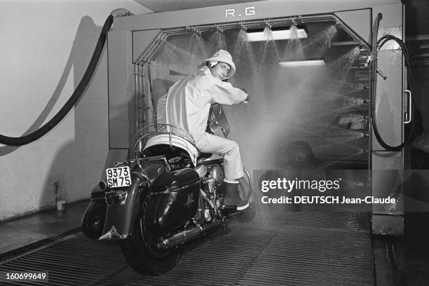 Close-up Of Jacques Dutronc. Jacques DUTRONC, dans un garage, sur une moto , en ciré imperméable et chapeau, prêt à entrer dans une station de lavage...