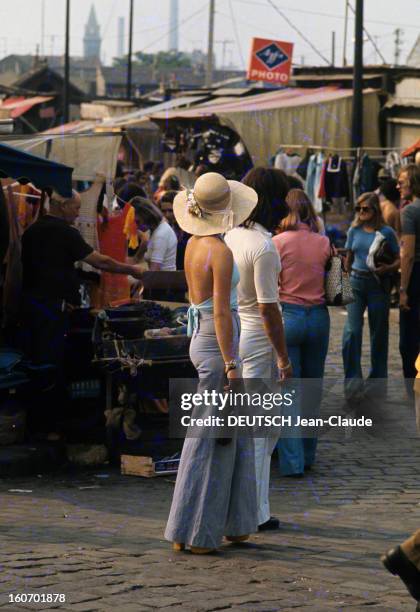 Fashion The Blue Jeans. France- 1973- L'empire du blue-jean. Sur un marché, une jeune femme coiffée d'un chapeau de paille à large bord enrubanné de...