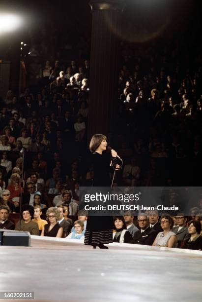 Close-up Of Mireille Mathieu In Gdr . RDA- 1972 - Mireille MATHIEU, souriante, vêtue d'une longue robe noire, chante un micro en main, sur une scène,...