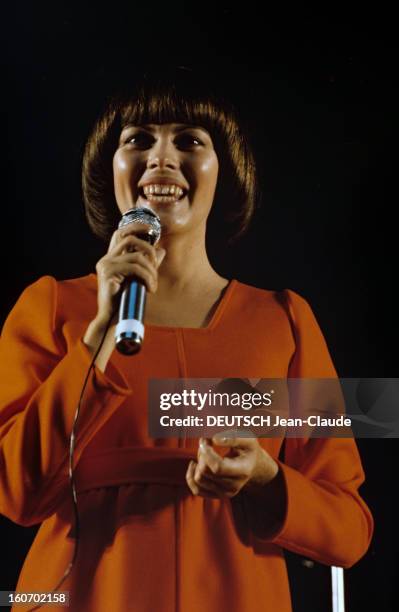 Close-up Of Mireille Mathieu In Gdr . RDA- 1972- Mireille MATHIEU, vêtue d'une longue robe orange à manches longues, chante sur scène, micro en main...