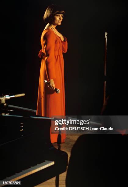 Close-up Of Mireille Mathieu In Gdr . RDA- 1972- Mireille MATHIEU, vêtue d'une longue robe orange à manches longues, se teint debout sur scène, micro...