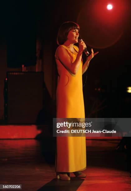 Close-up Of Mireille Mathieu In Gdr . RDA- 1972- Mireille MATHIEU, vêtue d'une longue robe orange à manches longues, chante debout sur scène, micro...