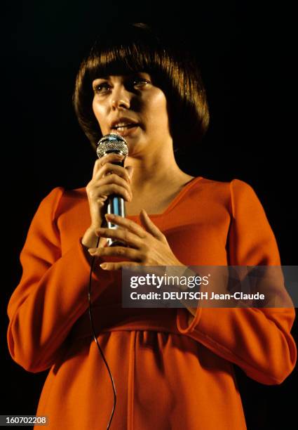 Close-up Of Mireille Mathieu In Gdr . RDA- 1972- Mireille MATHIEU, vêtue d'une longue robe orange à manches longues, chante sur scène, micro en main...